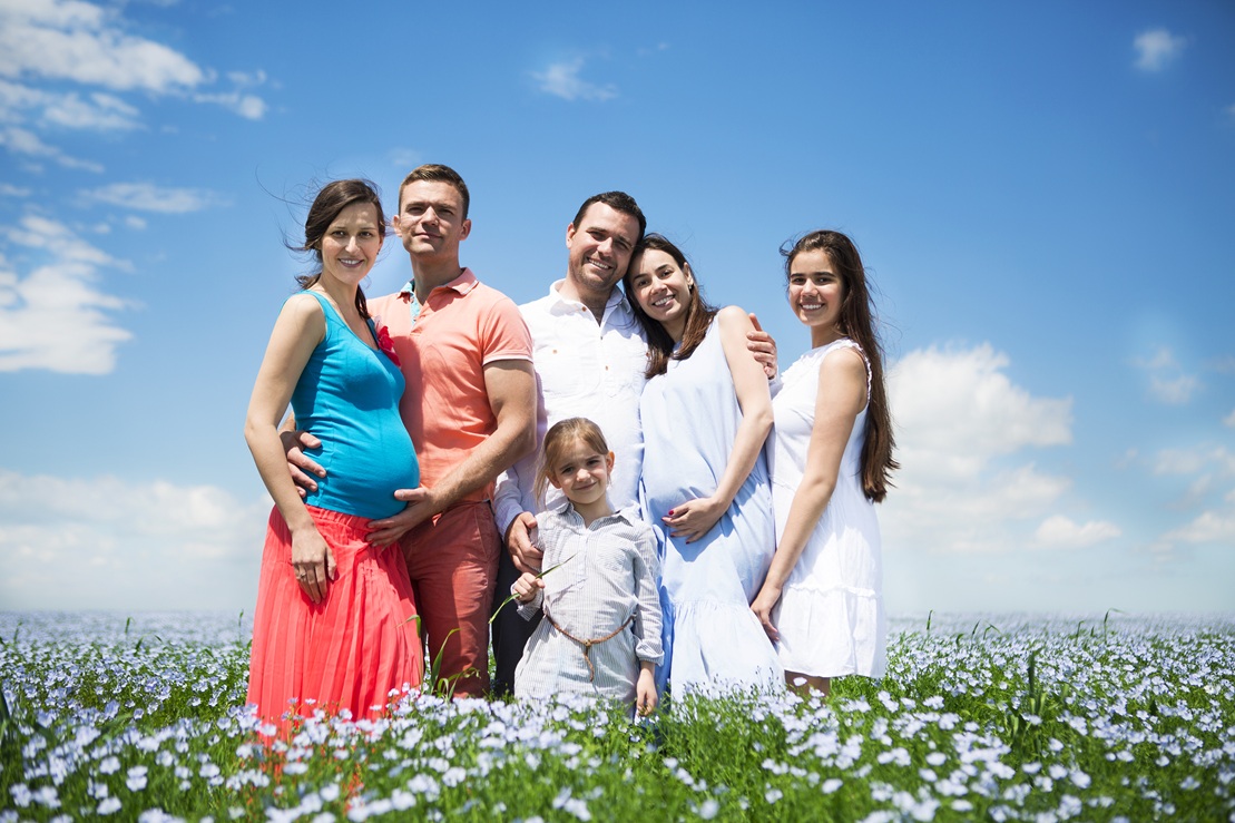 Portrait of a young big pregnant family in linen field. Summer time