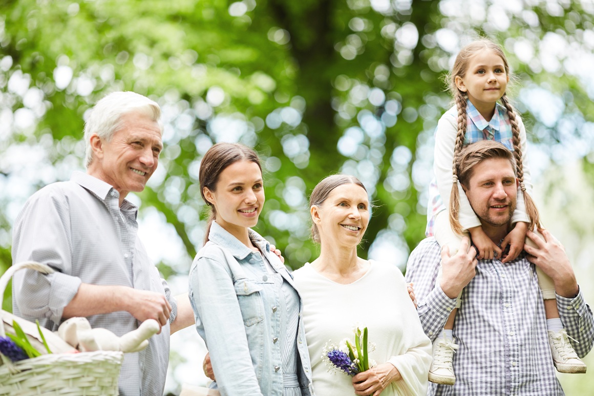 Two men and women and little girl on her father neck enjoying summer day in park